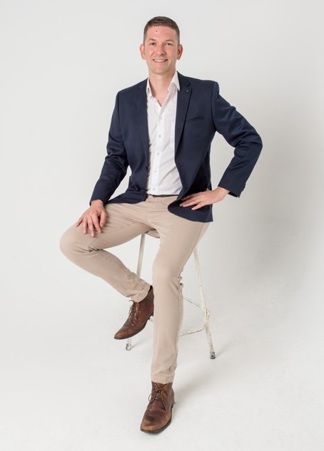 Steve Mucha, founder of Perth Property Deals, seated on a stool in a navy blazer against a light studio backdrop